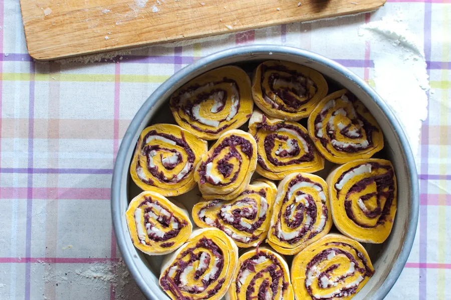 Rohe Teigrollen mit dunkelroten Rotweinzwiebeln und weißem Ziegenkäse, dicht nebeneinander in einer runden Springform.