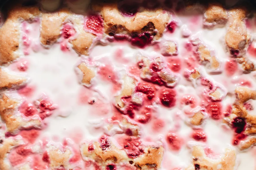 Zwei Teller mit himbeerroten Tres-Leches-Kuchenstücken und gelben Rosen auf einer karierten Tischdecke, dazu zwei Kinderhände mit Gabeln.