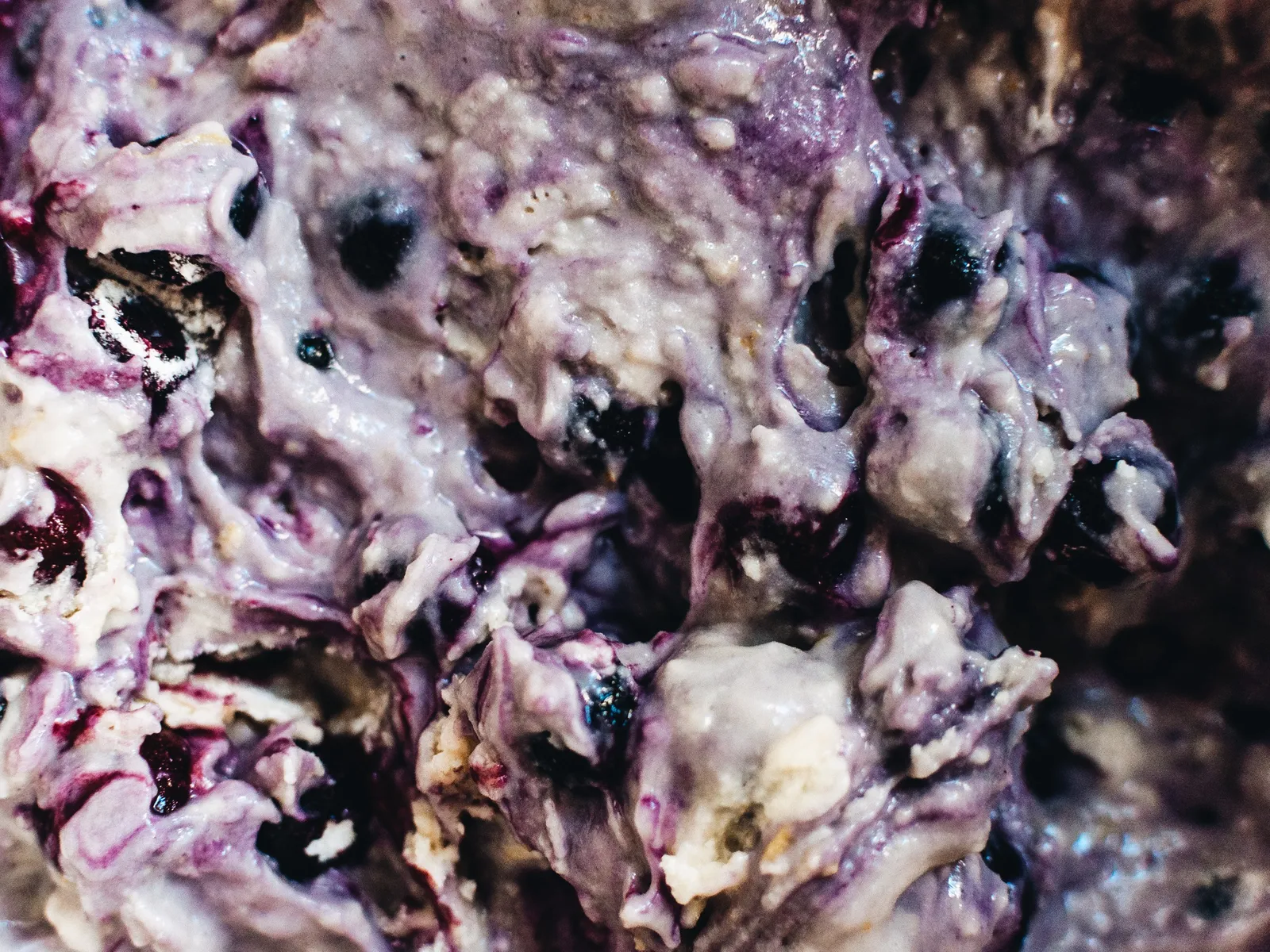 Muffinteig mit Blaubeeren in einer Schüssel, in violett-blau gefärbten Schlieren verrührt.