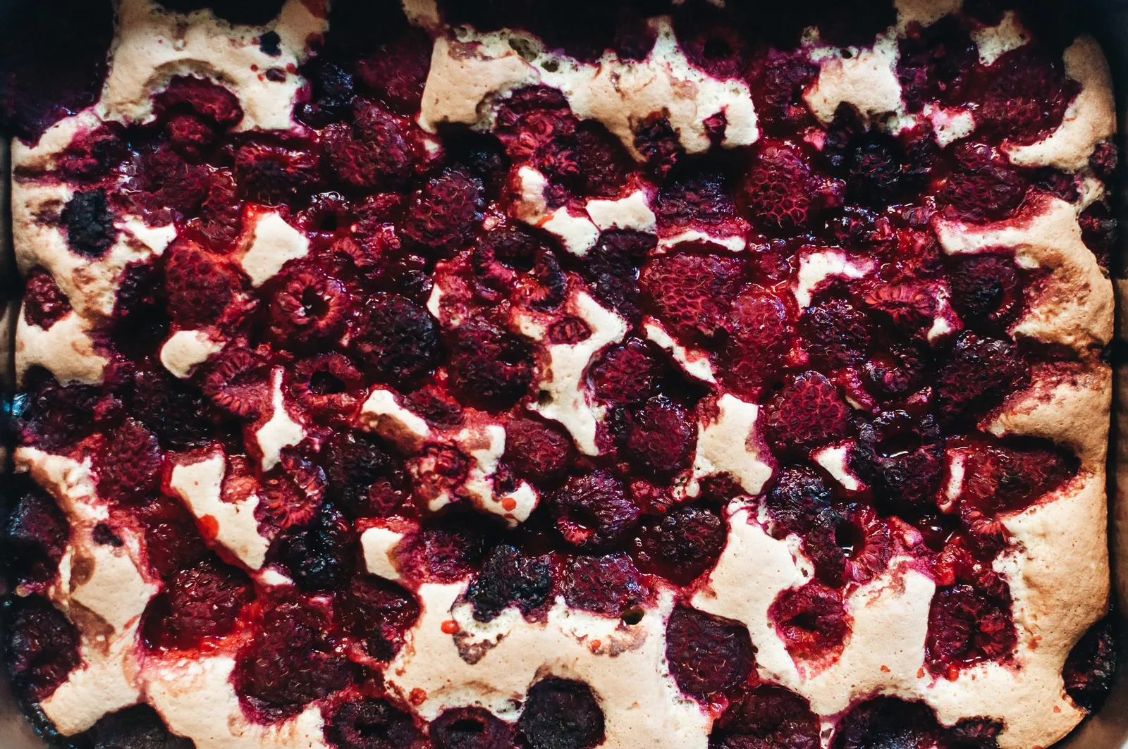 Luftig gebackener Kuchen von oben, dicht belegt mit dunkelroten Himbeeren, die im Ofen zu saftig-karamellisierten Flecken geschmolzen sind