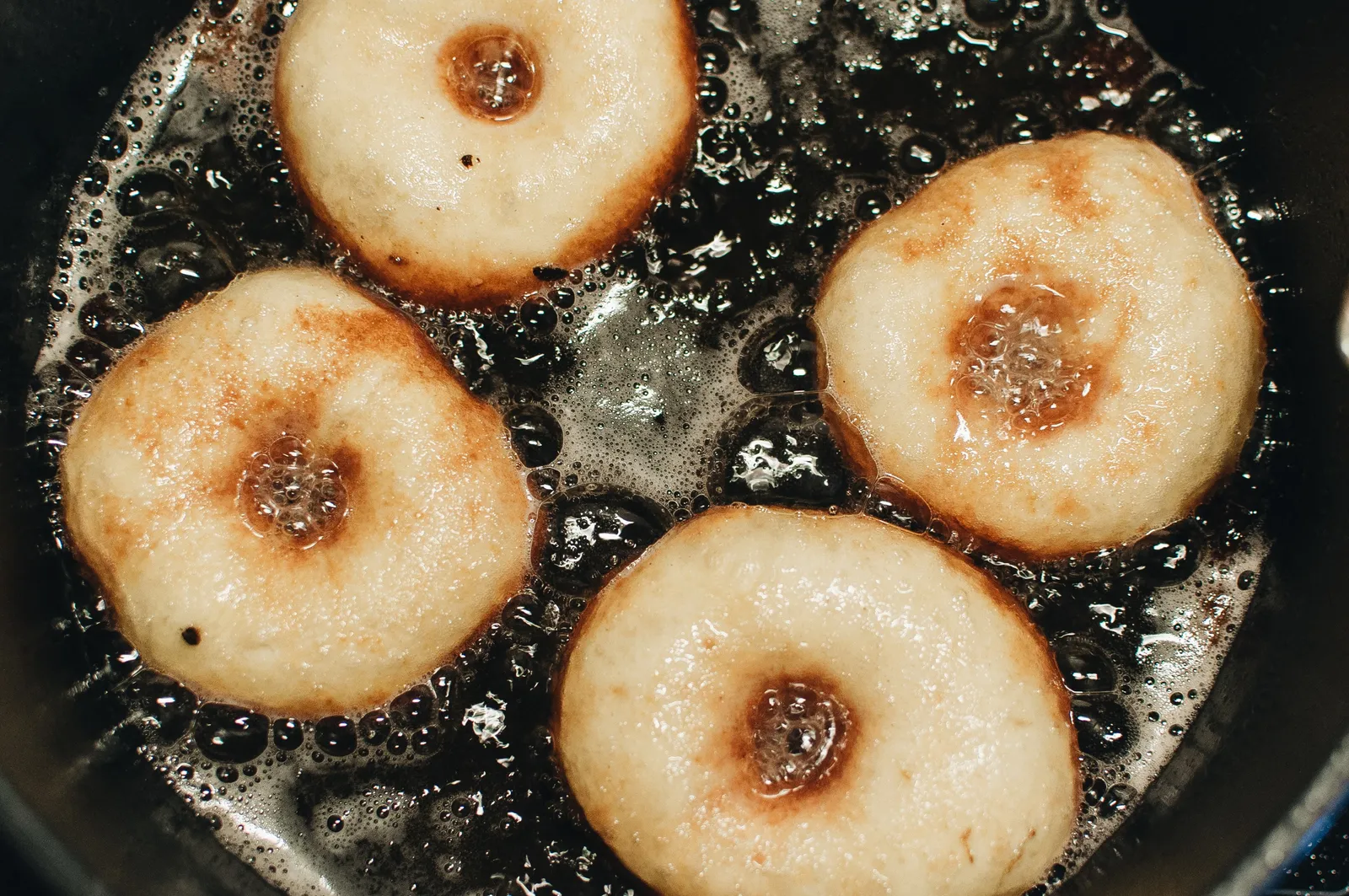 Vier Donuts schwimmen in sprudelndem heißem Öl und bräunen sich goldgelb von unten.