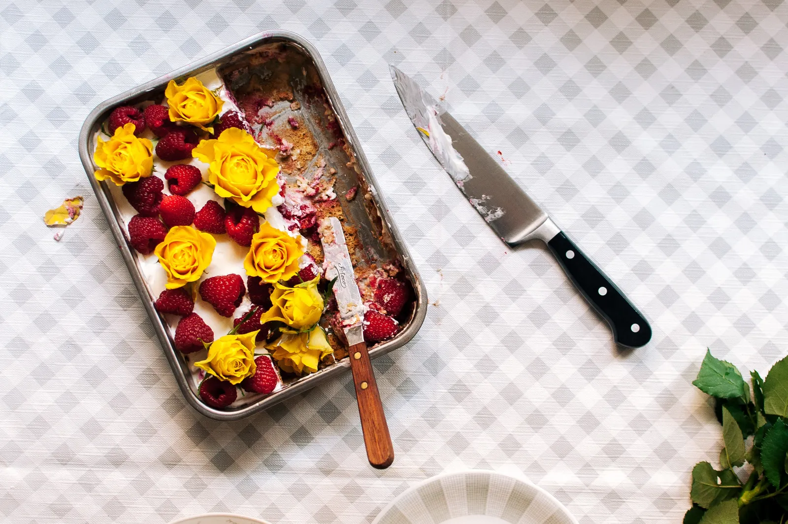 Ein Tres-Leches-Kuchen in der Backform, vollgesogen mit Milch und roten Himbeeren, mit einem großen Klecks Schlagsahne obenauf, auf einem hellgrauen Karostoff.