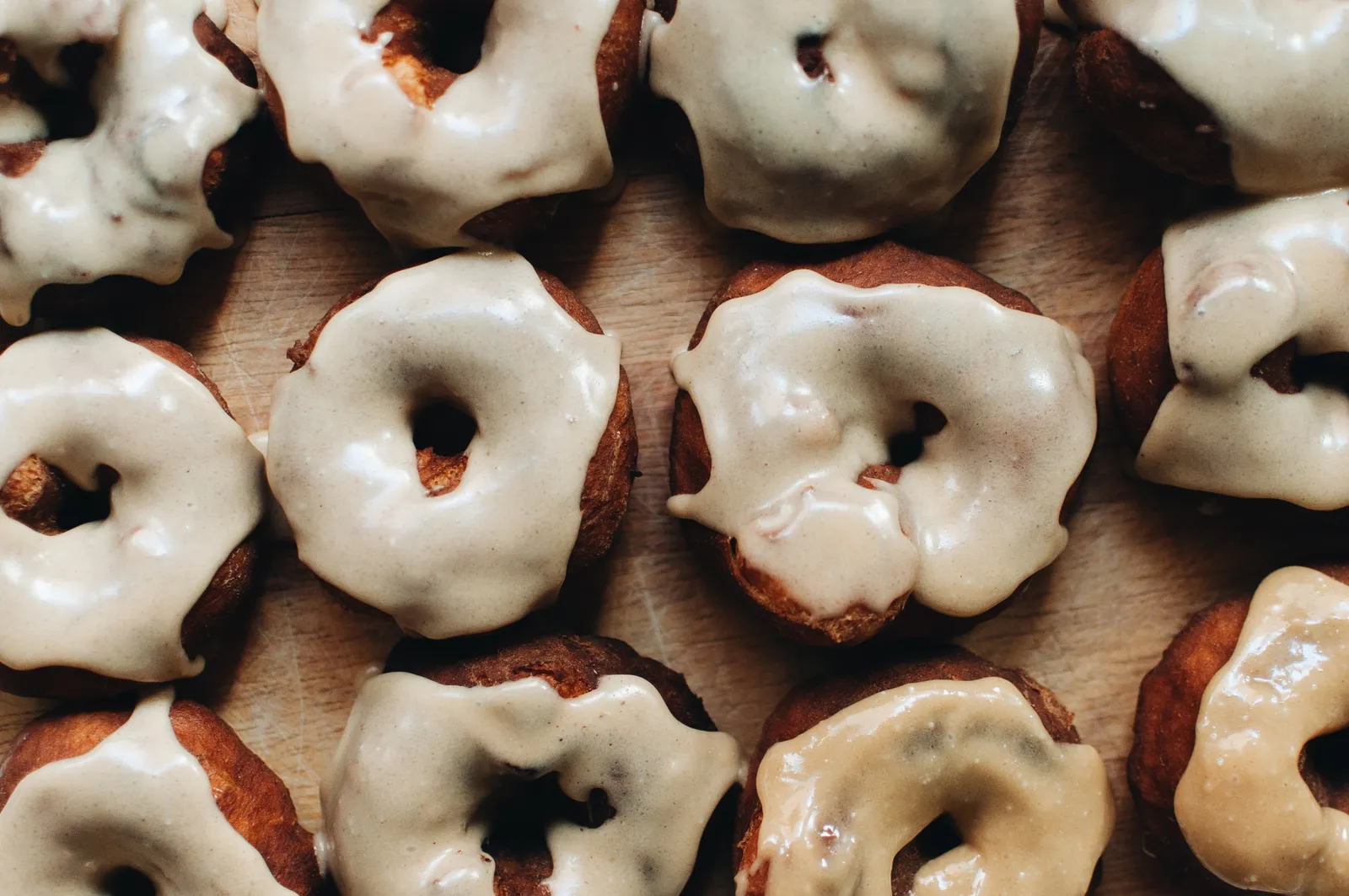 Mehrere goldbraune Laugendonuts mit cremiger Tahiniglasur, dicht nebeneinander auf einem Holzbrett.